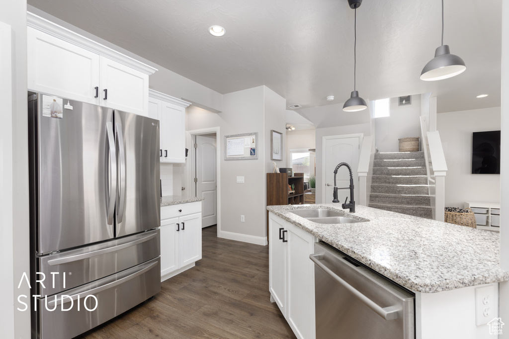 Kitchen with stainless steel appliances, white cabinetry, dark wood-type flooring, light stone counters, and decorative light fixtures