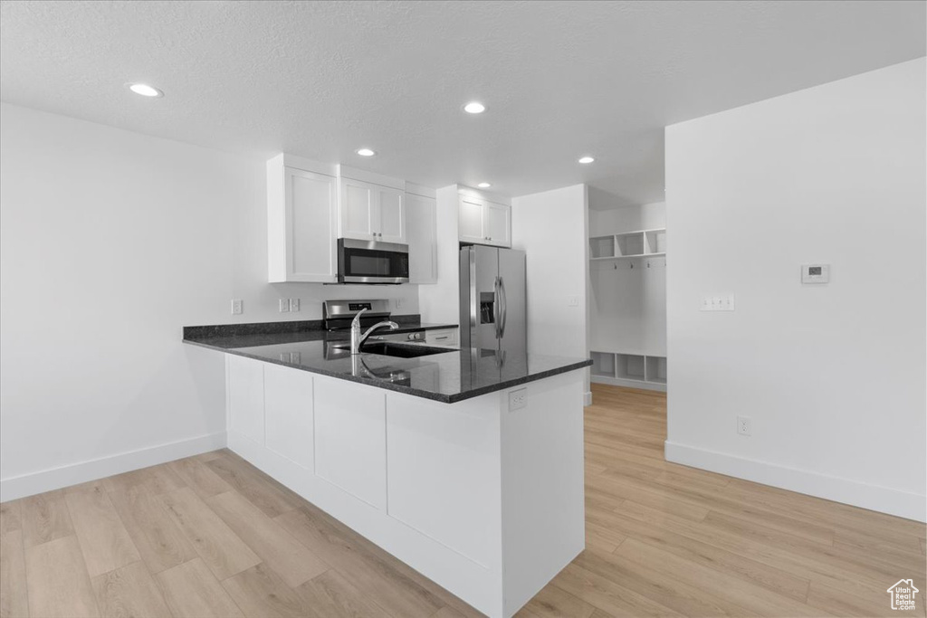 Kitchen featuring stainless steel appliances, a peninsula, light wood-style flooring, white cabinetry, and recessed lighting