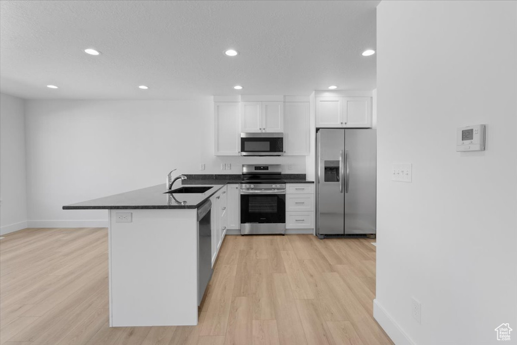 Kitchen with appliances with stainless steel finishes, a peninsula, dark countertops, recessed lighting, and light wood-type flooring