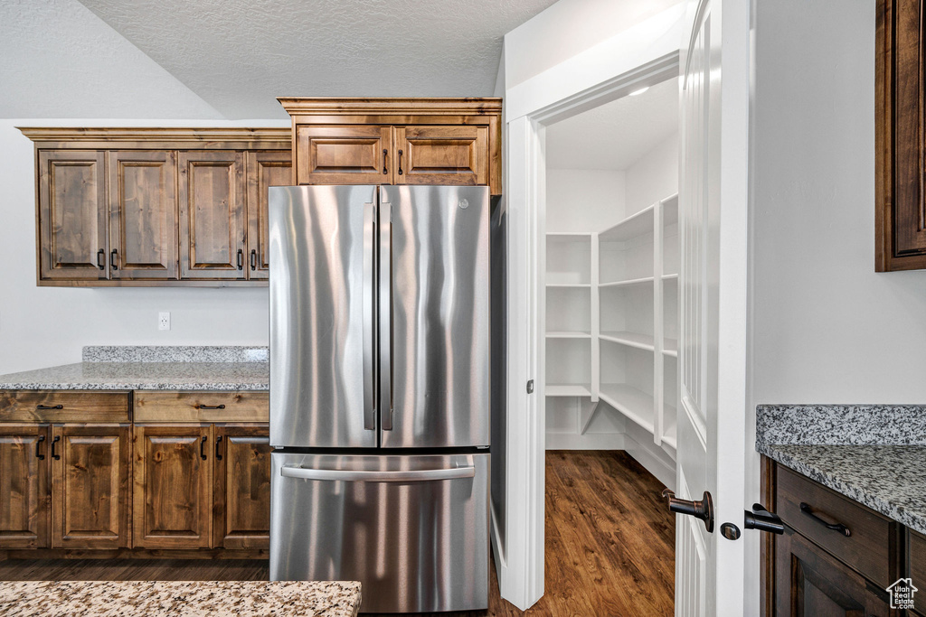 Kitchen featuring freestanding refrigerator, dark wood-style flooring, light stone countertops, and a textured ceiling