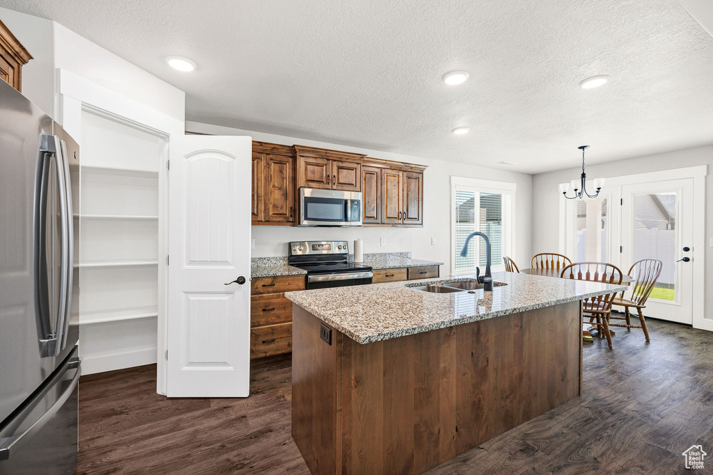 Kitchen featuring stainless steel appliances, dark wood finished floors, a chandelier, light stone countertops, and a textured ceiling
