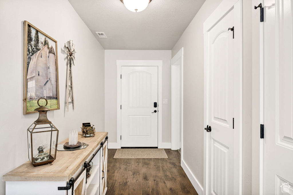 Doorway with dark wood-style flooring and baseboards