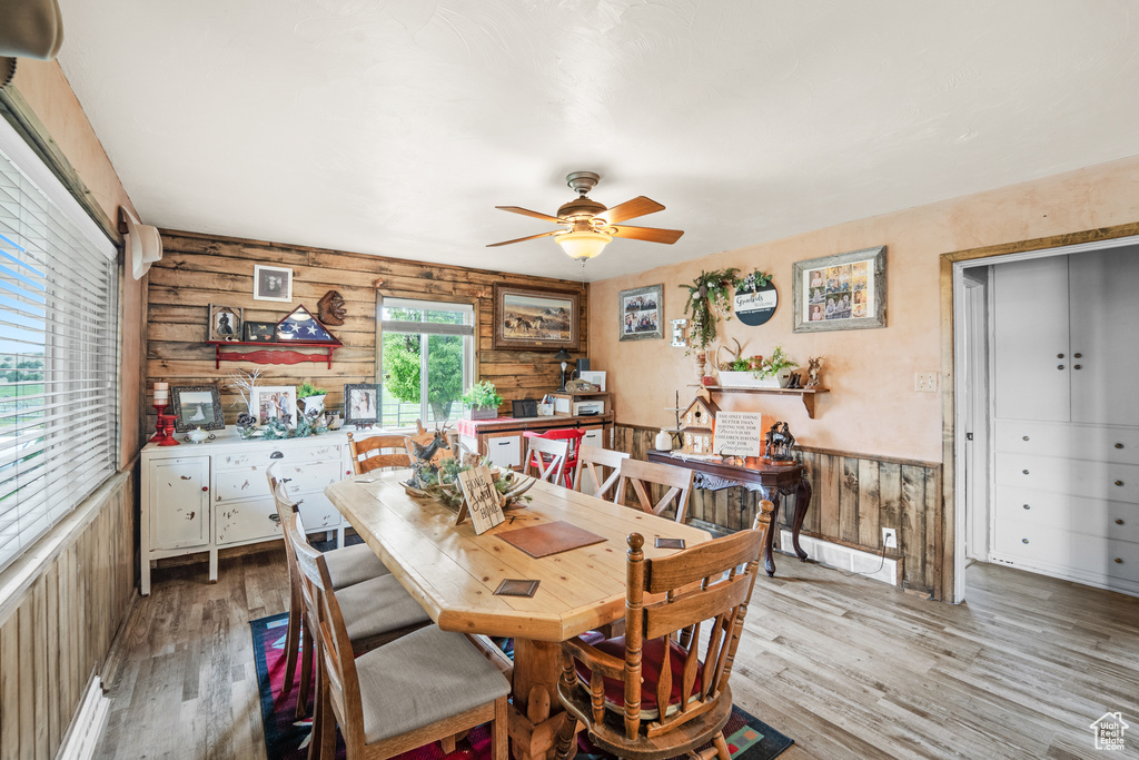Dining space with wood finished floors, a ceiling fan, wooden walls, and a wainscoted wall