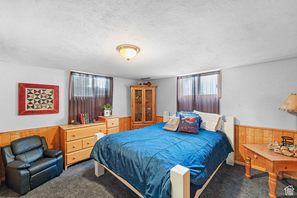 Bedroom with carpet flooring, a textured ceiling, wooden walls, and wainscoting