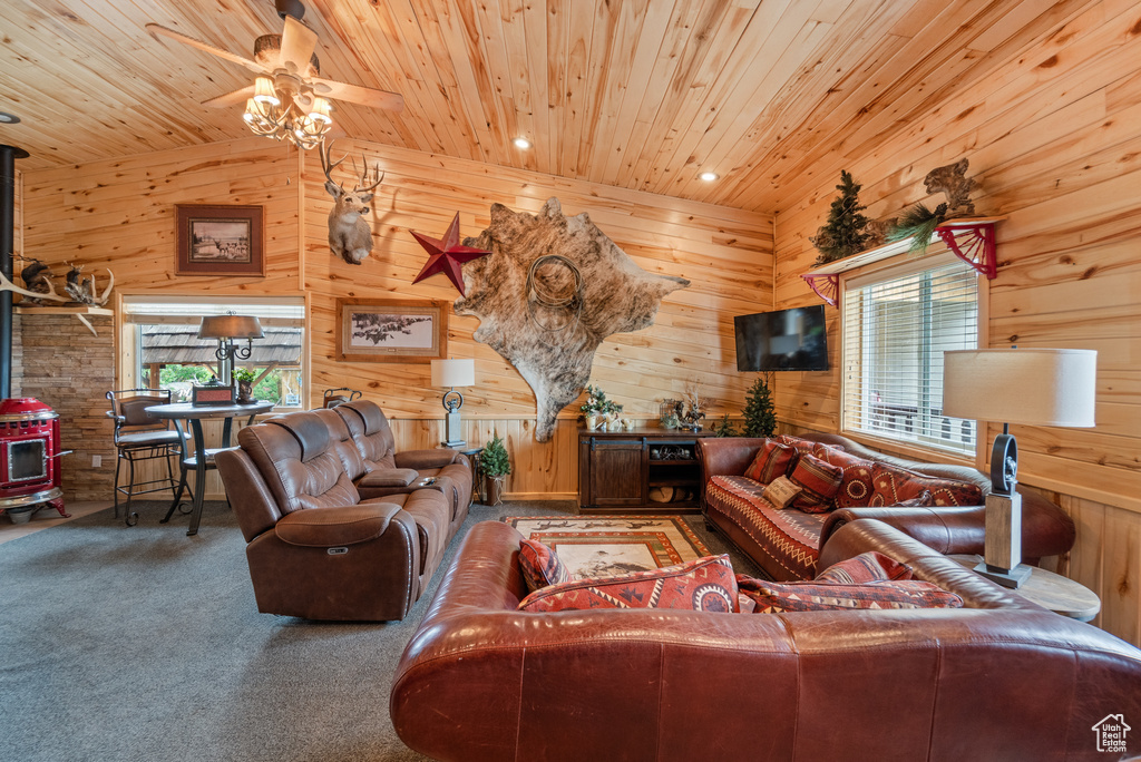 Living area featuring a wood stove, wood ceiling, plenty of natural light, a ceiling fan, and wooden walls