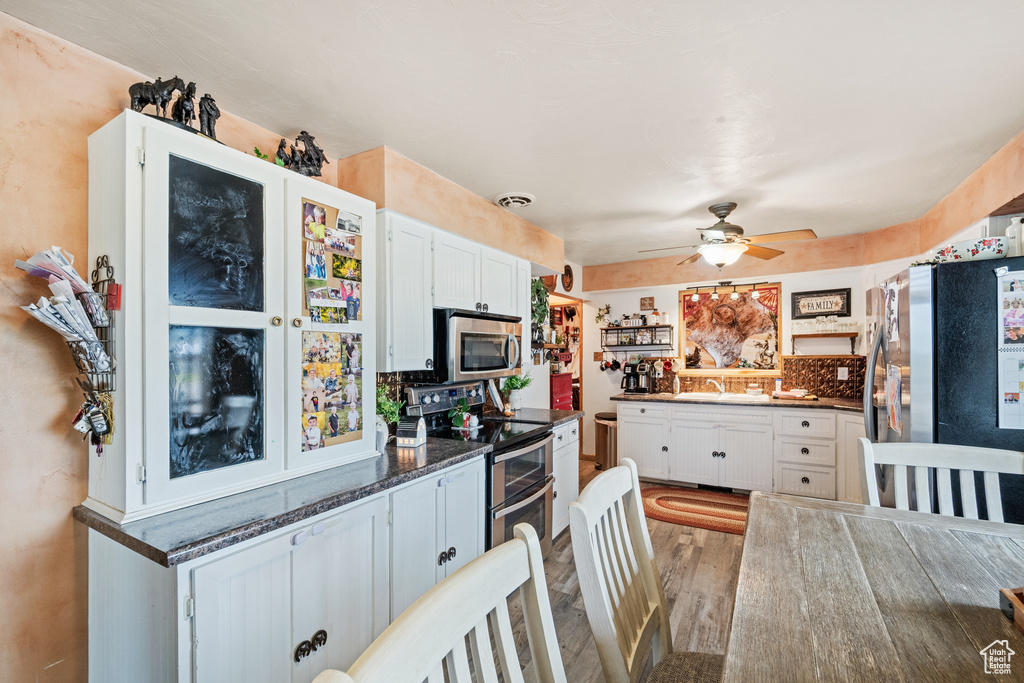 Kitchen with stainless steel appliances, a ceiling fan, dark countertops, white cabinets, and wood finished floors