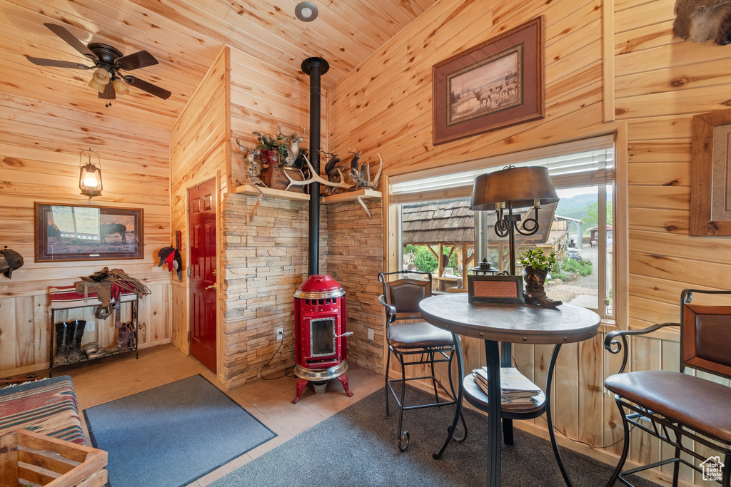 Dining area featuring a wood stove, wood walls, wooden ceiling, vaulted ceiling, and a ceiling fan