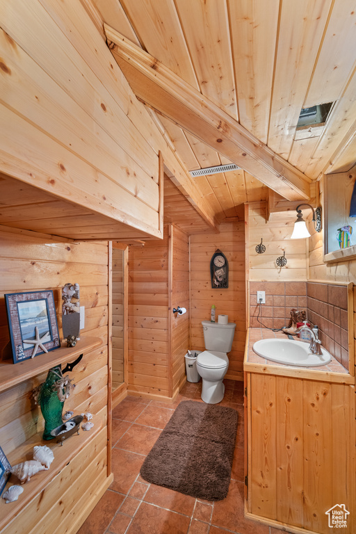 Bathroom with a wooden ceiling with exposed beams, vanity, and wooden walls