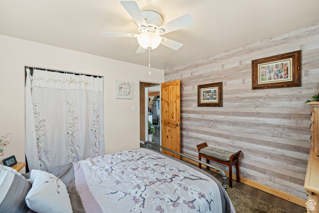 Bedroom featuring wood walls, an accent wall, wood finished floors, and a ceiling fan