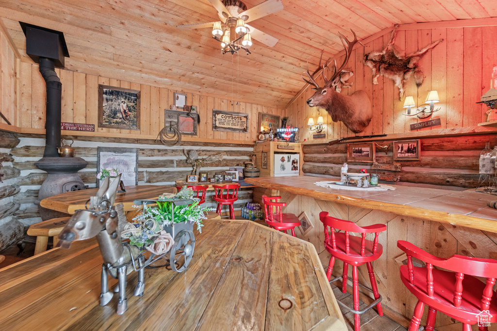 Dining room with lofted ceiling, a ceiling fan, wooden ceiling, wooden walls, and a wood stove