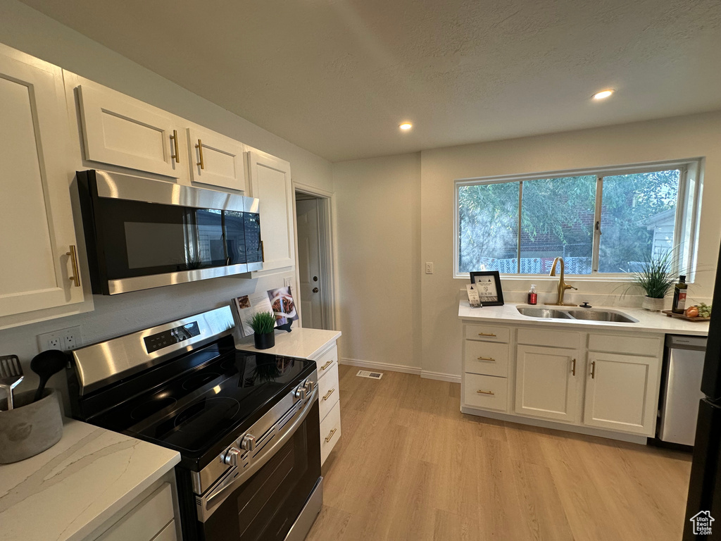Kitchen with appliances with stainless steel finishes, light wood-type flooring, white cabinets, and recessed lighting