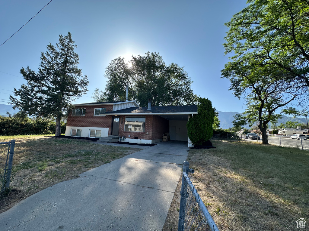 Split level home with brick siding, concrete driveway, an attached carport, and a chimney