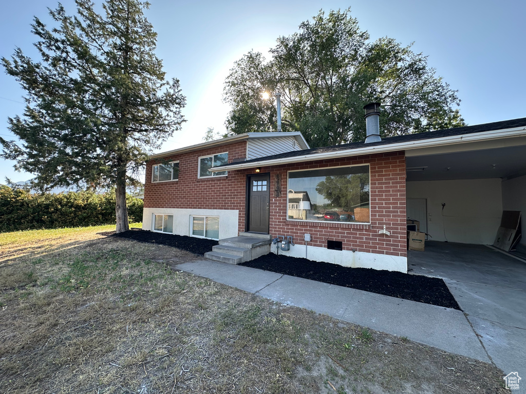Split level home featuring brick siding, concrete driveway, a carport, and a chimney
