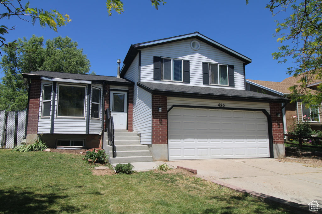Tri-level home featuring driveway, brick siding, an attached garage, and entry steps