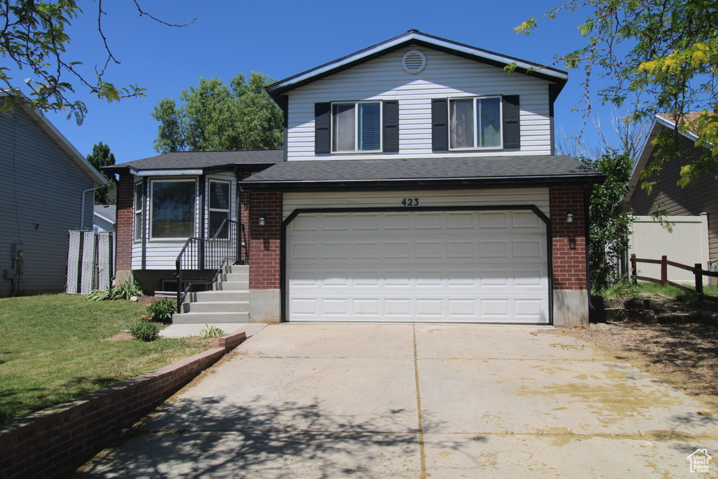 Tri-level home with brick siding, an attached garage, and driveway
