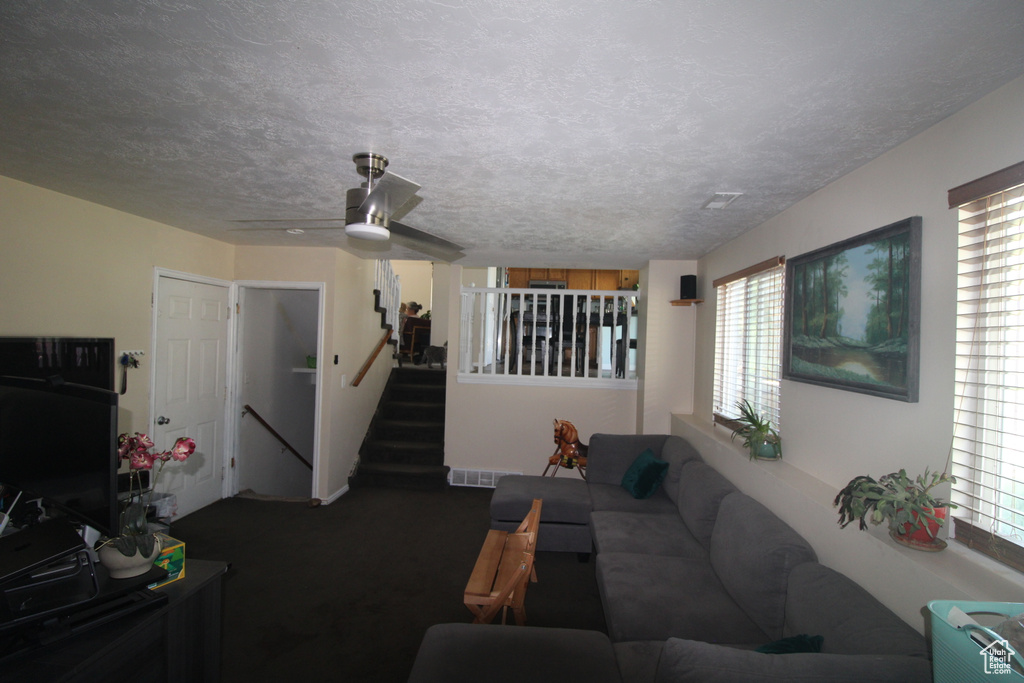 Carpeted living room featuring ceiling fan, a textured ceiling, and stairs