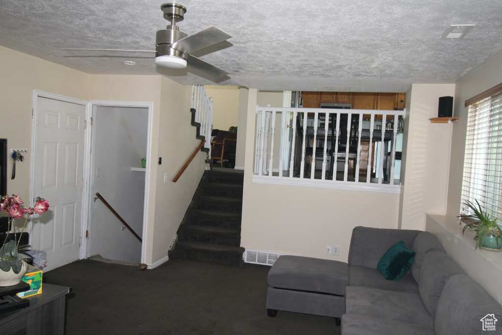 Carpeted living room with a ceiling fan, a textured ceiling, and stairway