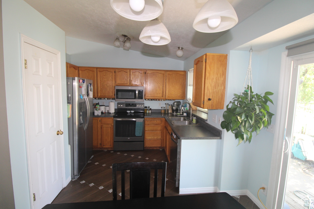 Kitchen with stainless steel appliances, dark countertops, brown cabinetry, dark wood-style flooring, and vaulted ceiling