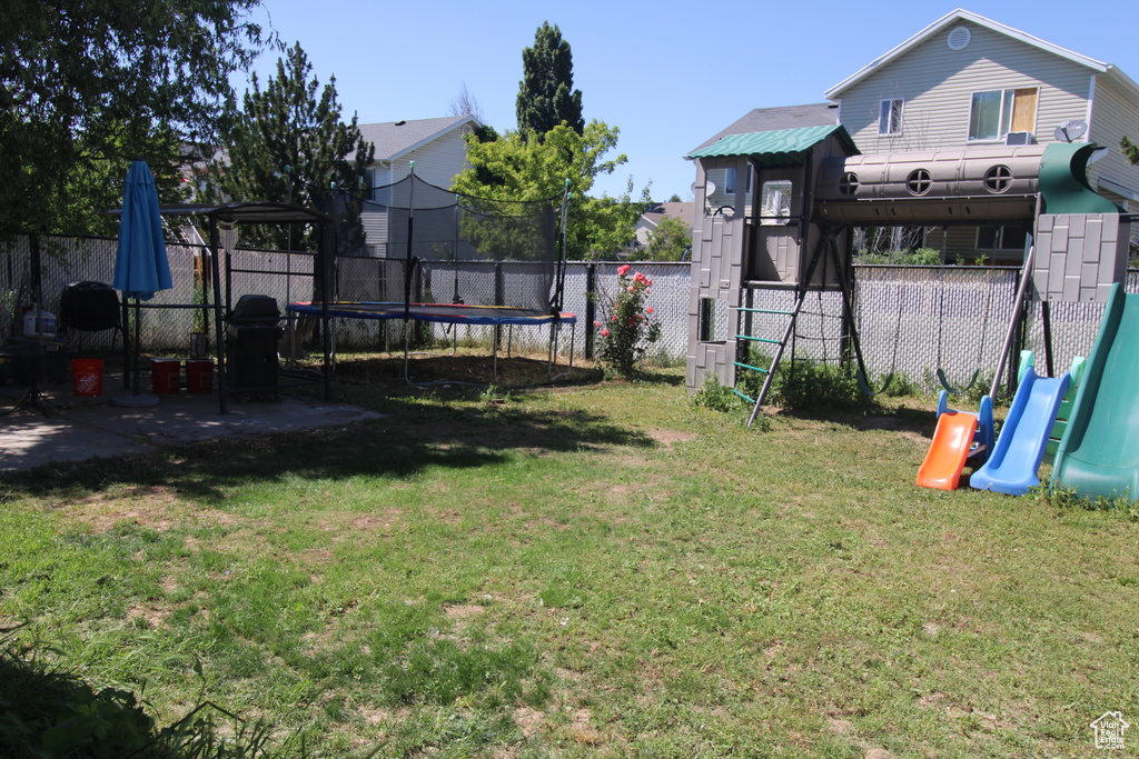 Fenced backyard featuring a trampoline and a playground