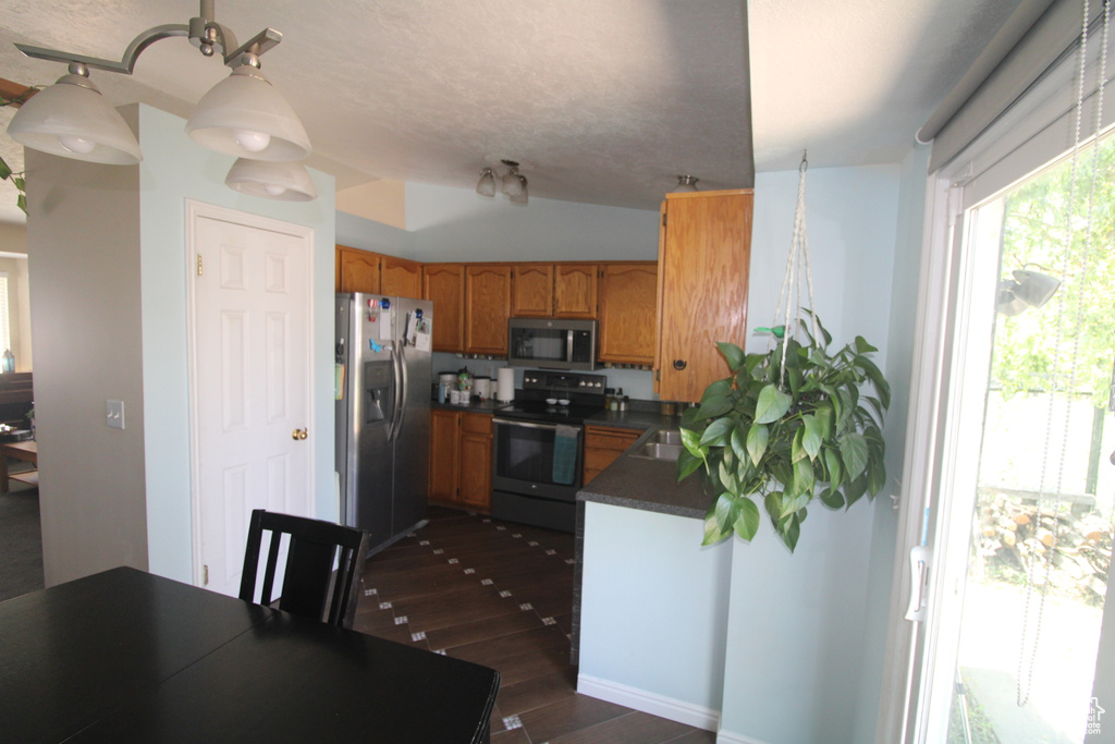 Kitchen featuring stainless steel appliances, dark countertops, dark wood-type flooring, and brown cabinets
