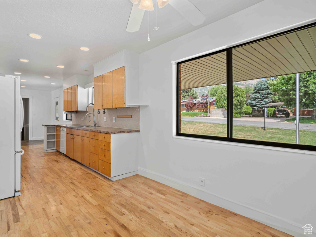 Kitchen with white appliances, light wood-style flooring, backsplash, ceiling fan, and recessed lighting