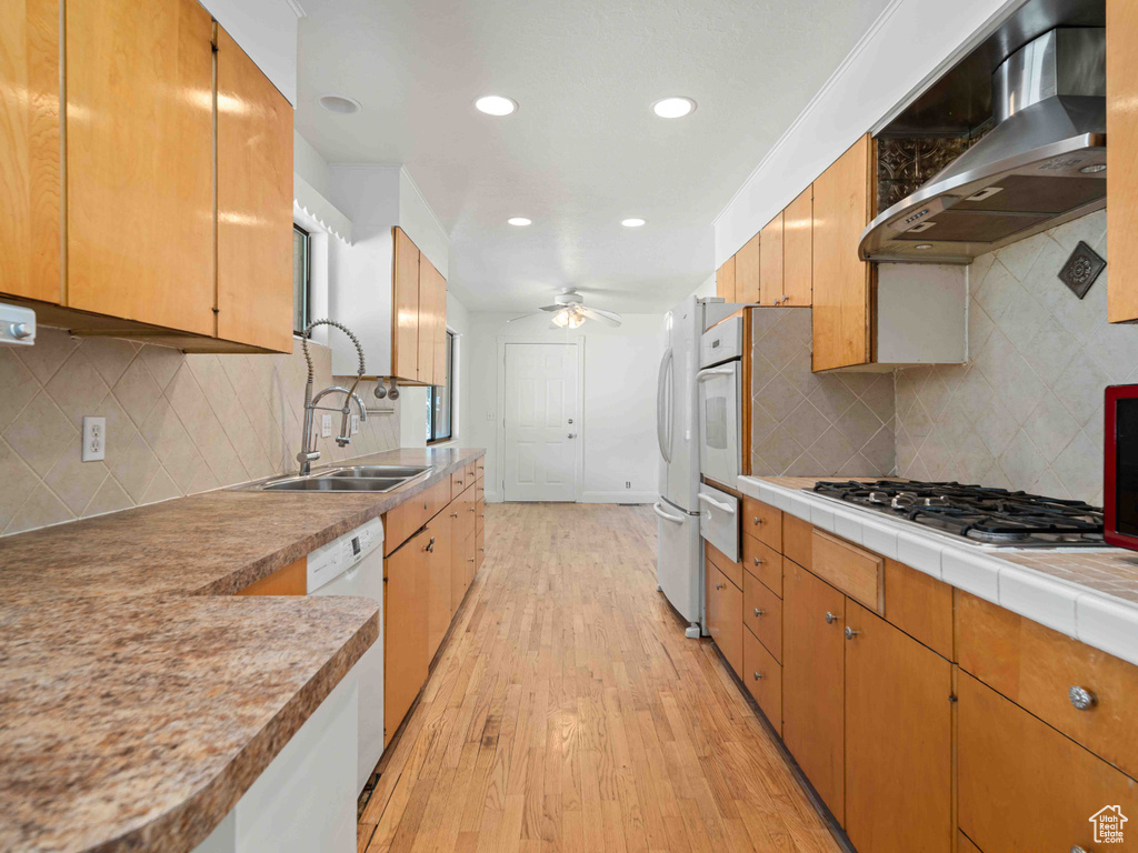 Kitchen featuring wall chimney range hood, white appliances, ceiling fan, light wood finished floors, and tasteful backsplash