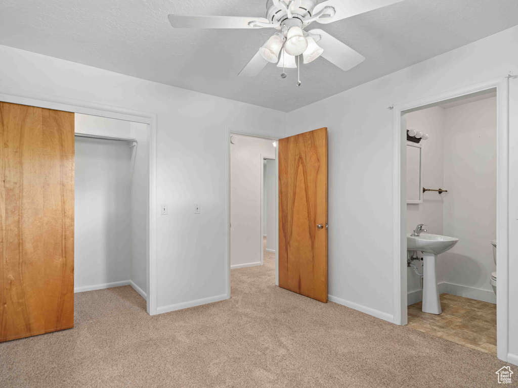 Unfurnished bedroom featuring carpet floors, a closet, ensuite bath, and a ceiling fan
