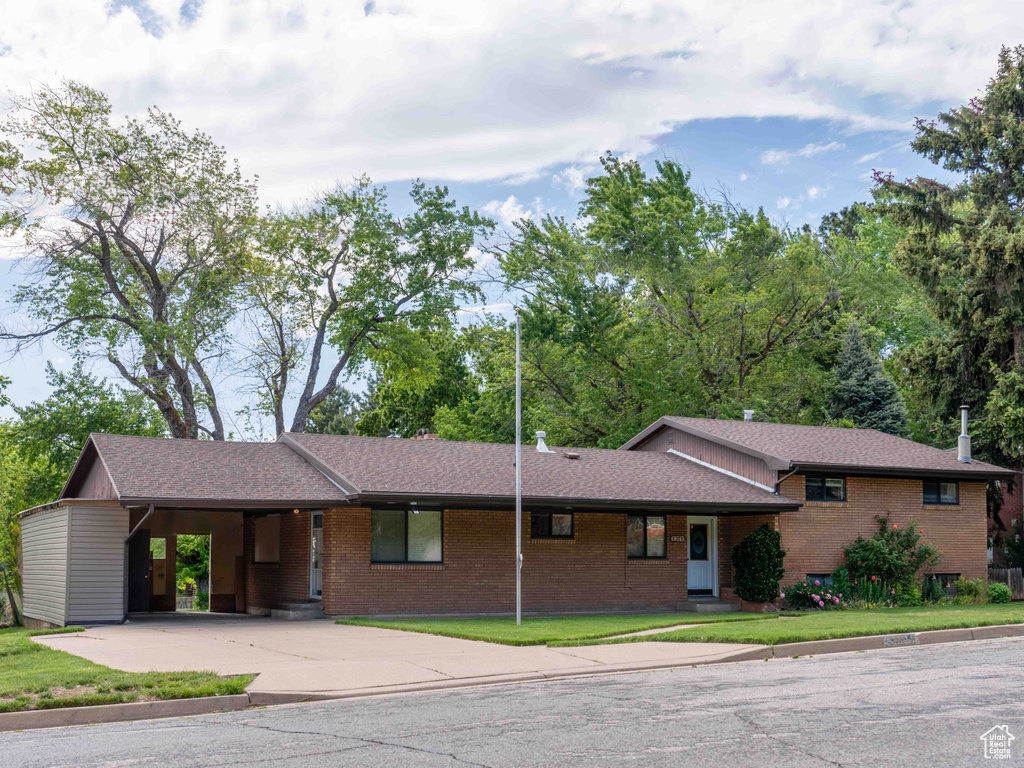 View of front facade featuring concrete driveway, brick siding, an attached carport, a shingled roof, and a front lawn