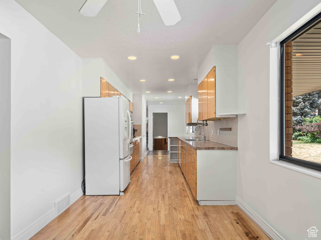 Kitchen featuring white fridge with ice dispenser, light wood-type flooring, recessed lighting, a ceiling fan, and dark countertops