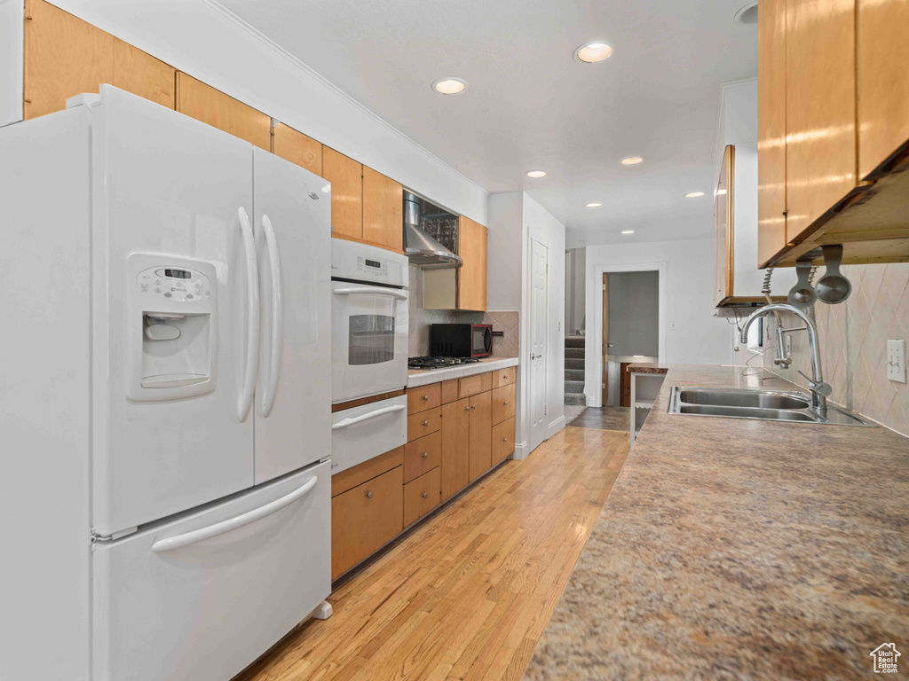 Kitchen featuring white appliances, a warming drawer, backsplash, light wood-style floors, and recessed lighting