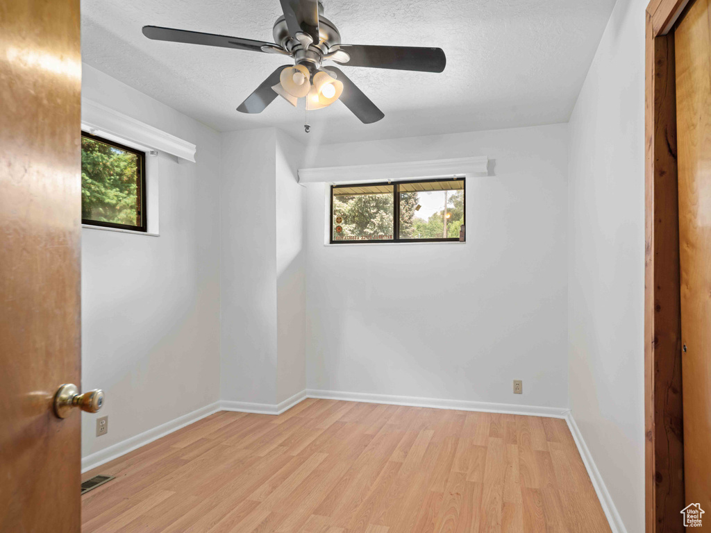 Spare room with light wood finished floors, healthy amount of natural light, a ceiling fan, and a textured ceiling