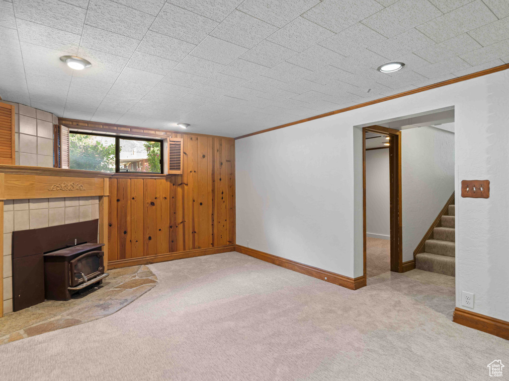 Unfurnished living room with a wood stove, carpet flooring, stairway, wooden walls, and crown molding