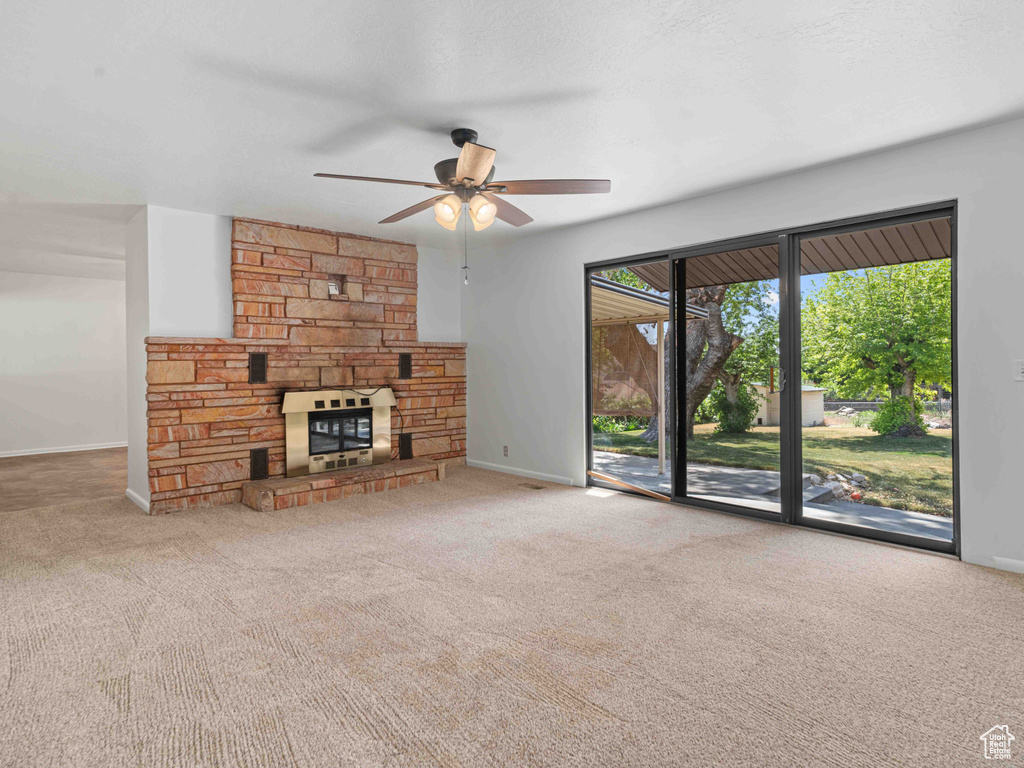 Unfurnished living room with ceiling fan, carpet flooring, and a stone fireplace