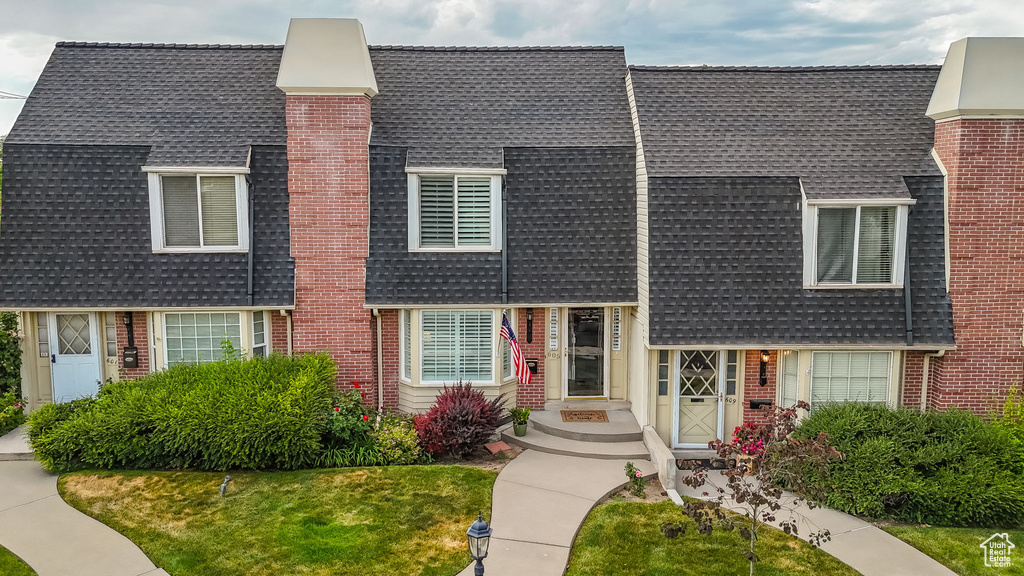 View of front of house featuring roof with shingles, brick siding, a front yard, and a chimney