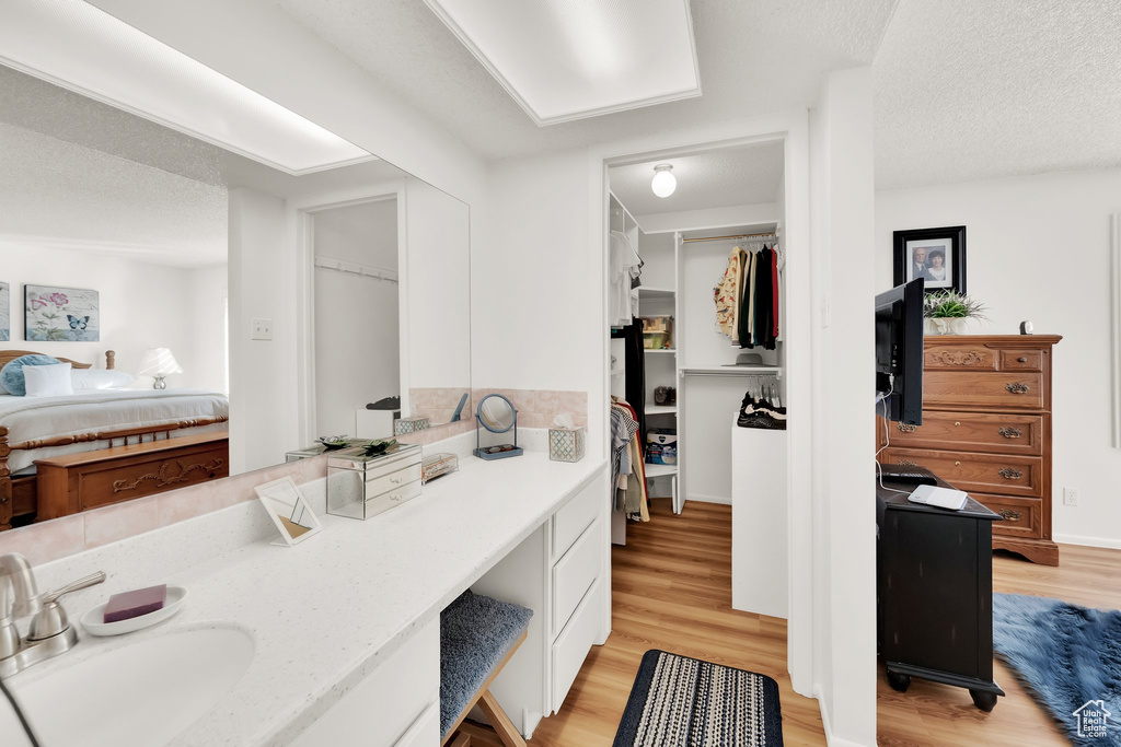 Ensuite bathroom with wood finished floors, a walk in closet, vanity, and a textured ceiling