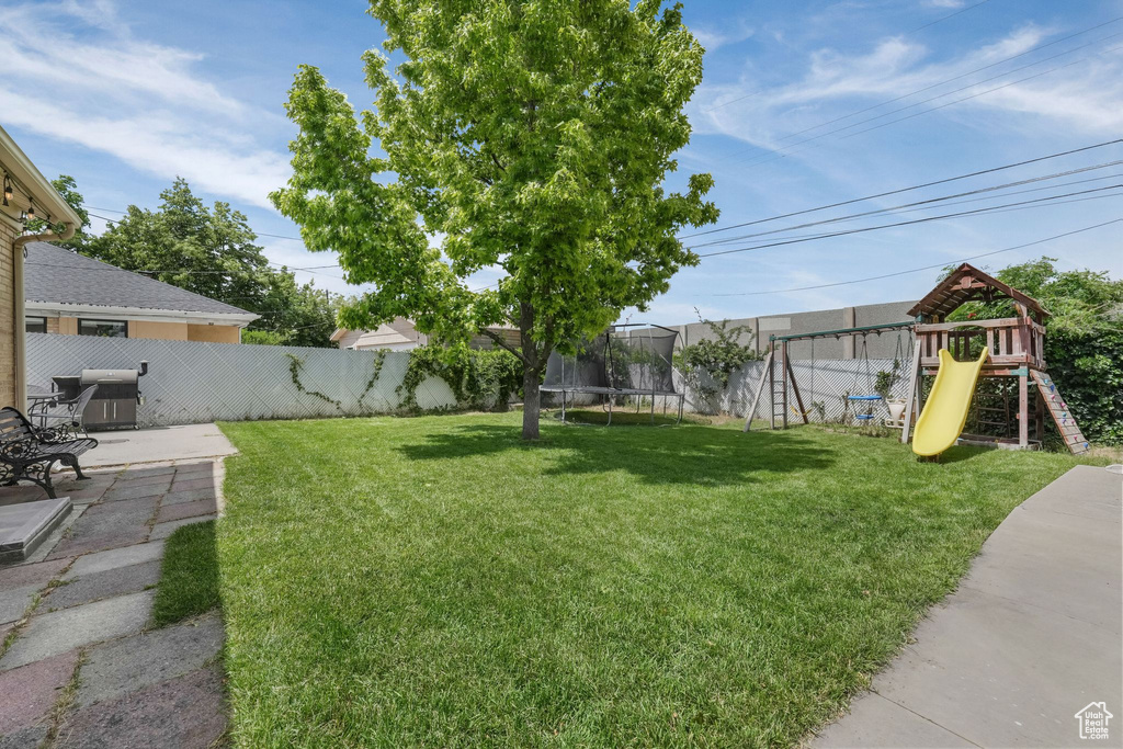 Fenced backyard with a trampoline, a playground, and a patio area