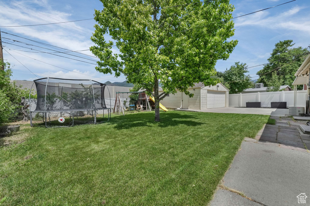 View of yard featuring a trampoline, concrete driveway, an outdoor structure, a playground, and a garage