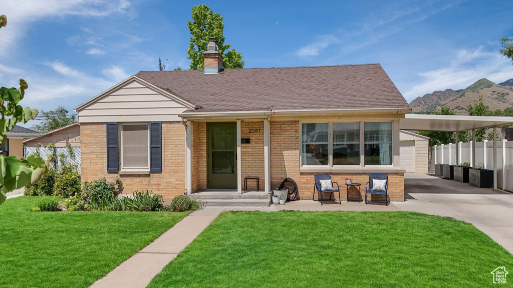 View of front of property featuring driveway, brick siding, a carport, and a chimney