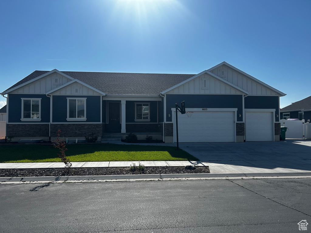 View of front of house with board and batten siding, a front lawn, a garage, roof with shingles, and driveway