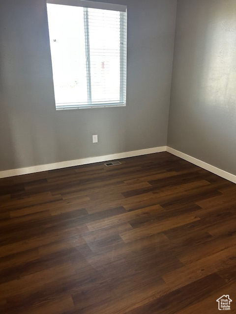 Spare room with baseboards and dark wood-type flooring