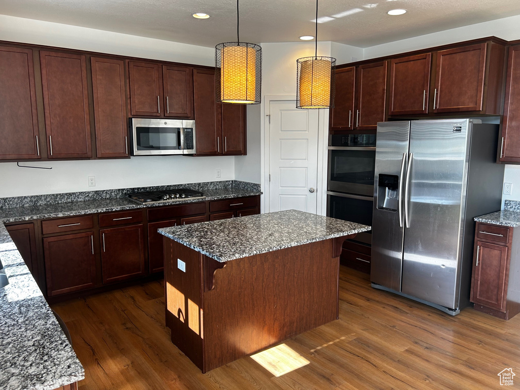 Kitchen featuring stainless steel appliances, dark wood finished floors, dark stone counters, recessed lighting, and a kitchen island
