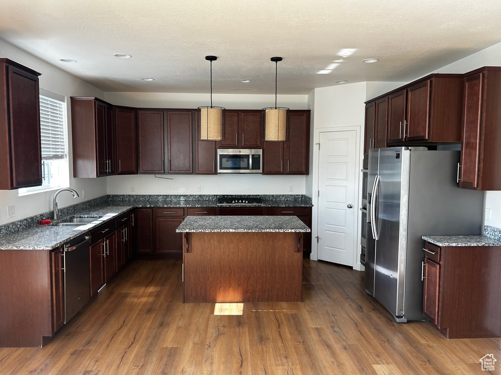 Kitchen featuring stainless steel appliances, a kitchen island, dark wood-style floors, dark stone counters, and recessed lighting