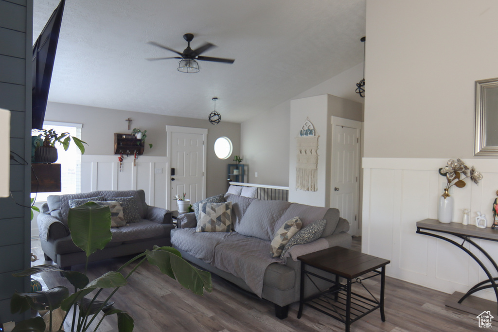 Living room featuring wood finished floors, a ceiling fan, vaulted ceiling, a decorative wall, and a wainscoted wall