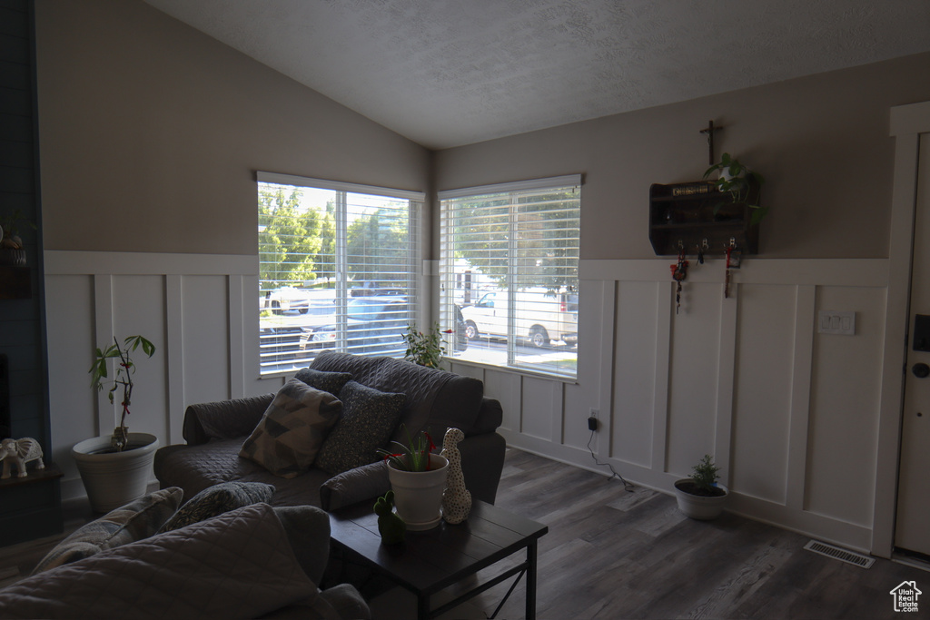 Living area featuring a decorative wall, lofted ceiling, wood finished floors, wainscoting, and a textured ceiling