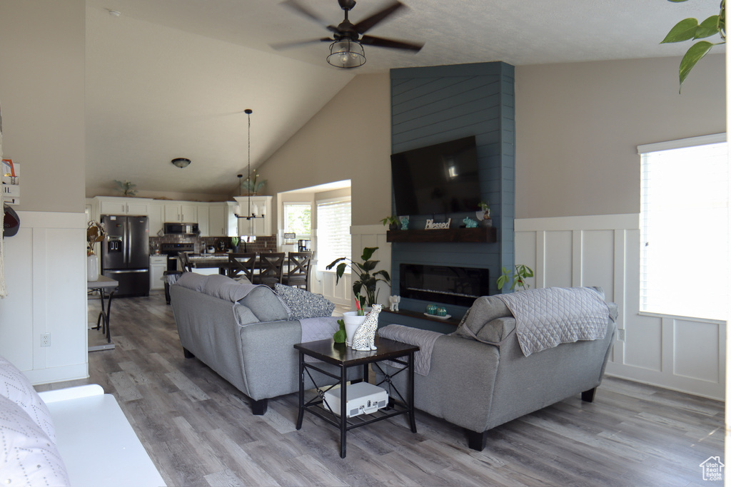 Living area featuring ceiling fan, a decorative wall, light wood-type flooring, a wainscoted wall, and high vaulted ceiling