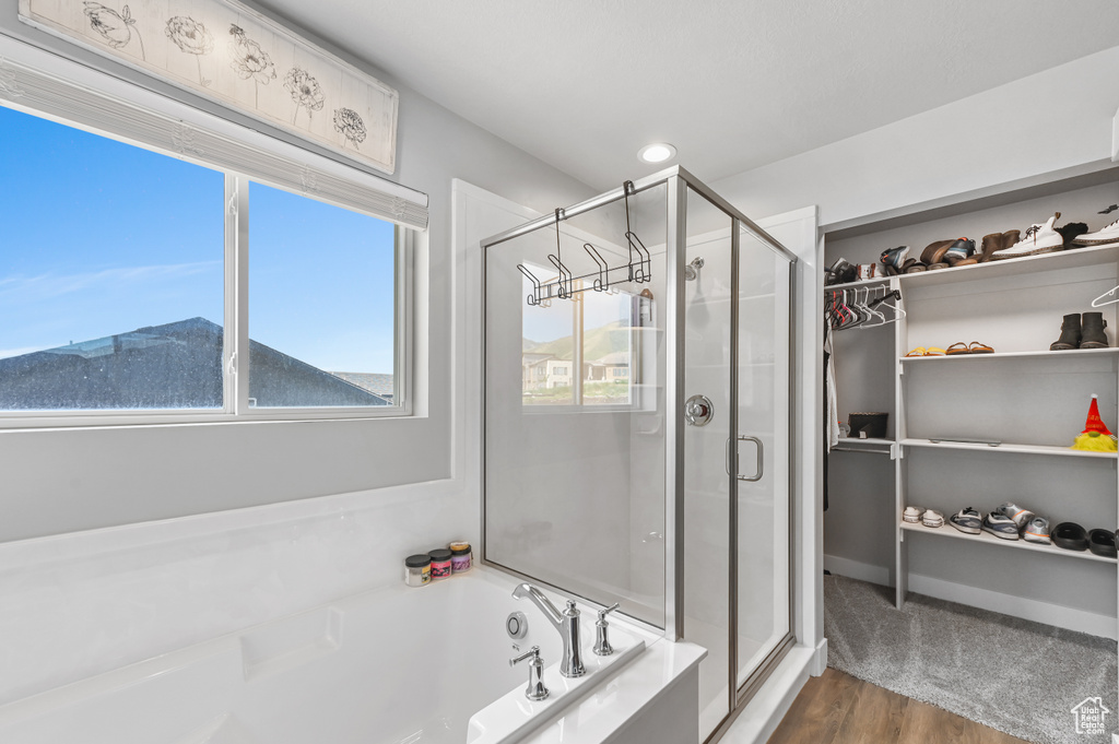 Bathroom with a stall shower, a bath, a spacious closet, wood finished floors, and recessed lighting