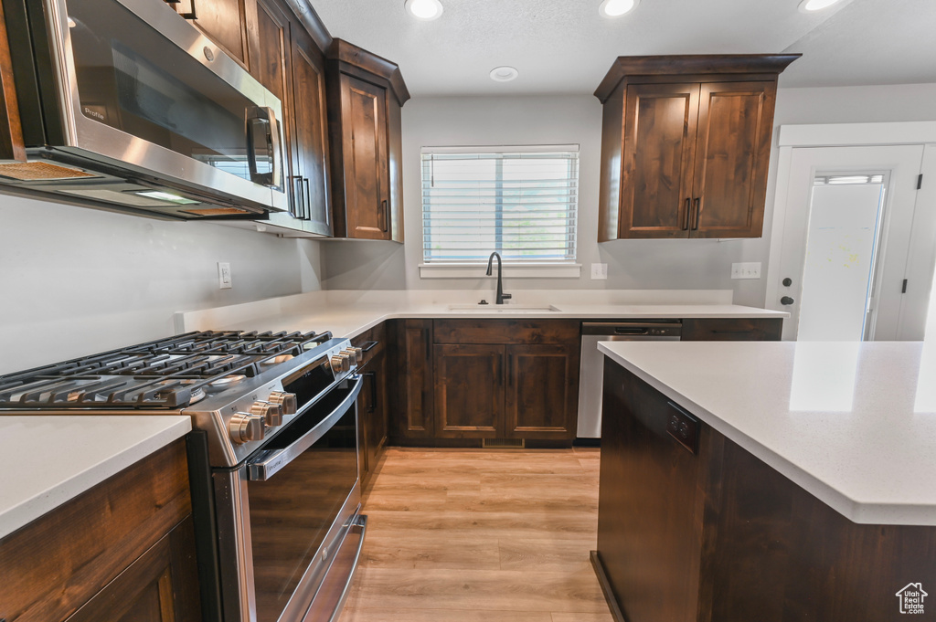 Kitchen with stainless steel appliances, light countertops, recessed lighting, dark brown cabinets, and light wood finished floors