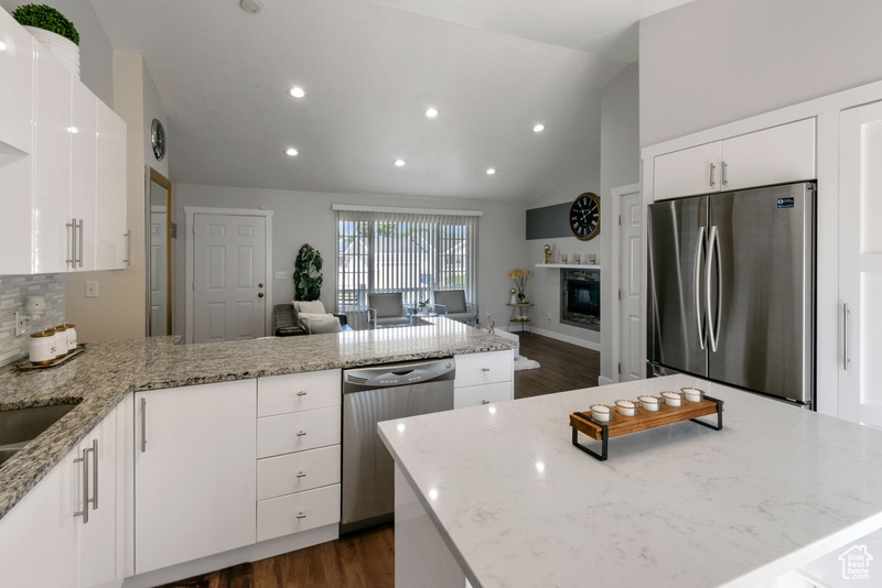Kitchen with stainless steel appliances, a peninsula, dark wood-type flooring, vaulted ceiling, and light stone countertops