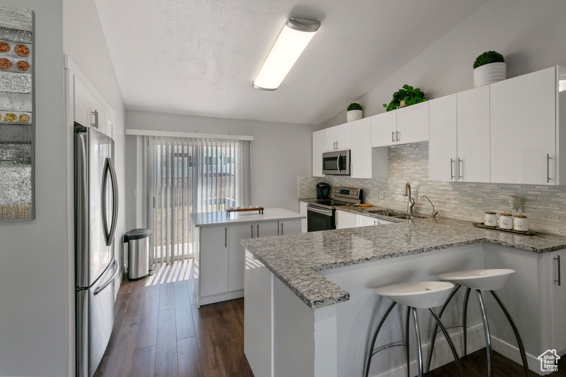 Kitchen with appliances with stainless steel finishes, lofted ceiling, a peninsula, decorative backsplash, and a kitchen island
