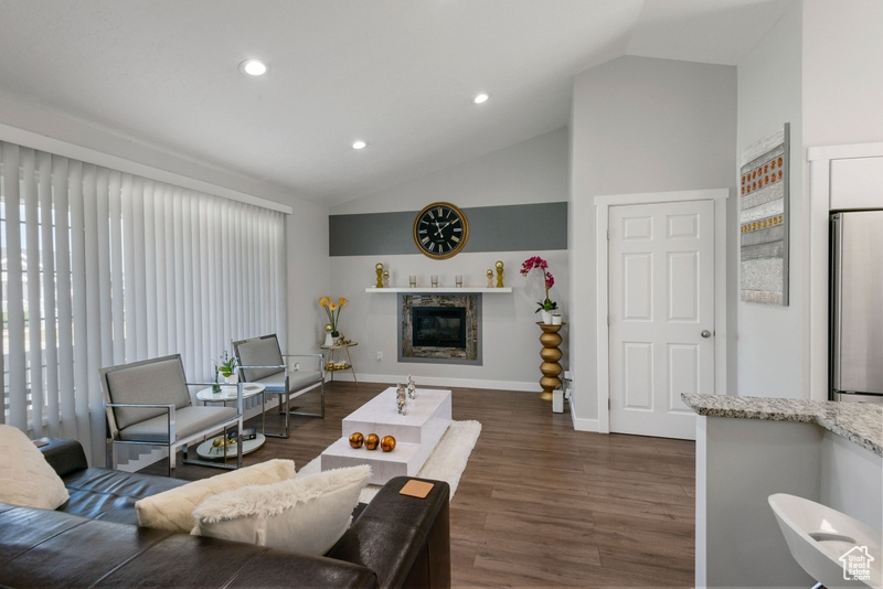 Living room with lofted ceiling, dark wood-type flooring, recessed lighting, and a glass covered fireplace